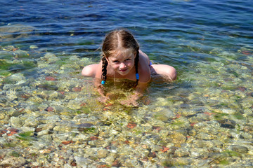 girl with pigtails sitting in the pose of a frog on the sea 