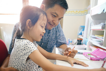 Young daughter and her father helping homework school project at home.