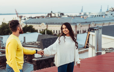 Loving young couple is standing on the roof of the house.