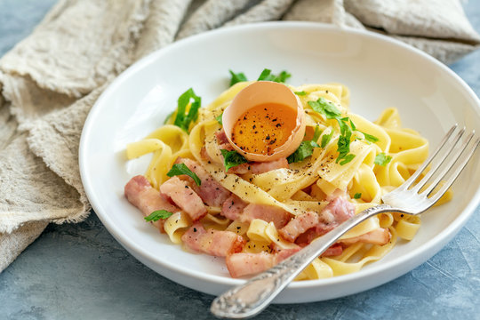 Pasta carbonara with egg yolk in a white plate.