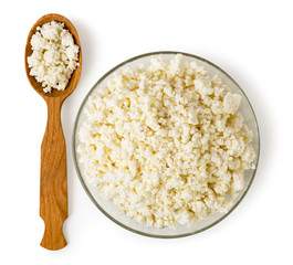 Cottage cheese in a glass plate and a wooden spoon on a white. The view from the top.