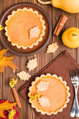 Pumpkin pie with cinnamon and cookies on brown napkins on wooden background with autumn yellow leaves.