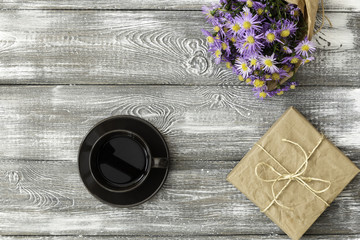 Gift or present box wrapped in kraft paper, cup coffe and flower on gray table from above. Flat lay styling. Copy space for text.