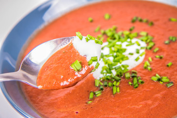 Beetroot cream soup decorated with yogurt and chives being eaten with a spoon