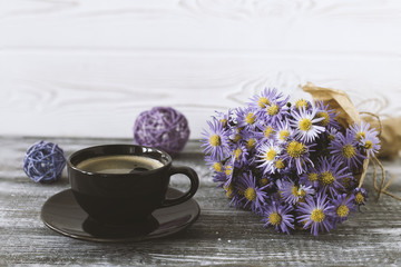 Romantic background with a cup of coffee, a bouquet of purple flowers in craft paper on a gray wooden table