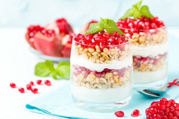 Pomegranate parfait - sweet organic layered dessert with granola flakes, yogurt and red ripe fruit seeds.