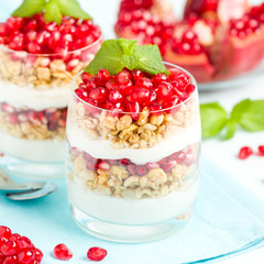 Pomegranate parfait - sweet organic layered dessert with granola flakes, yogurt and red ripe fruit seeds.
