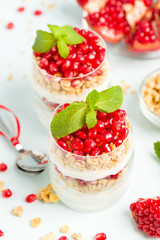 Pomegranate parfait - sweet organic layered dessert with granola flakes, yogurt and red ripe fruit seeds.