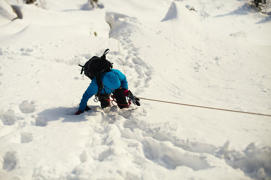 Climber pulls on a rope railing on a snowy mountain slope.