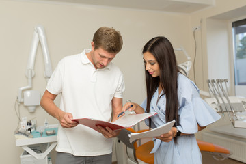 Obraz premium doctor and his assistant looking in folder with paper. Dental office background