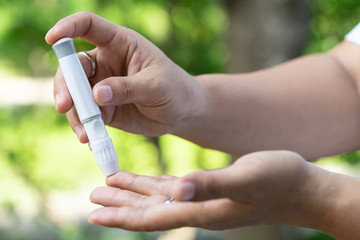 Close up of asian woman hands using lancet on finger to check blood sugar level by glucose meter, Healthcare medical and check up, diabetes, glycemia, and people concept