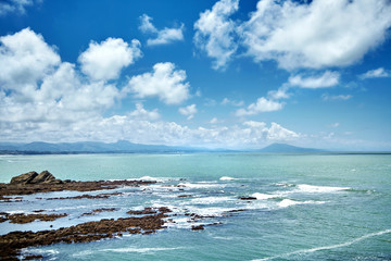 Rocky coastline. Seascape. Waves with white foam and cliff. Coast of the Atlantic Ocean in southern France. Mountains on the horizon. Blue sky with clouds