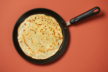 Crepe closeup, thin pancake on a frying pan, brown background