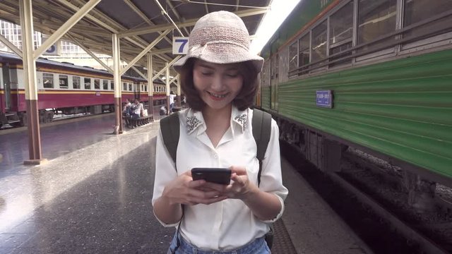 Slow motion - Traveler backpacker Asian woman travel in Bangkok, Thailand. Happy young female using smartphone for talking, reading and texting at train station.