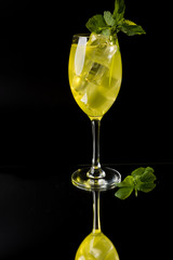 yellow cocktail with ice and mint reflected on black background