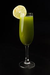 green cocktail with slice of lime on black background