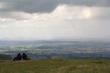 Fototapeta na wymiar A pair of hikers sit down for lunch at the edge of High Cup Nick in the Pennines on a typical English summer’s day