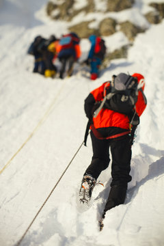 Climber climbing a rope railing on a snowy slope. Tilt-shift effect.