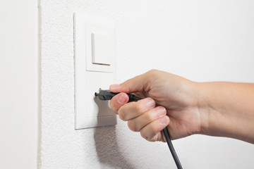 A woman's hand pulls a black cord from the socket.