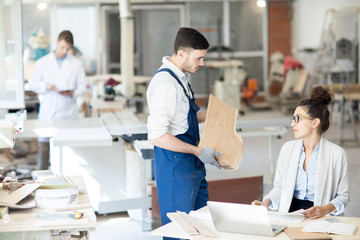 Obraz premium Young engineer in overalls showing piece of wood to analyst during consultation in workshop