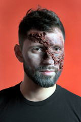 The guy in the black t-shirt with makeup in the style of Halloween. Vertical portrait of a young man with ragged facial wounds. Festive party. Red background.