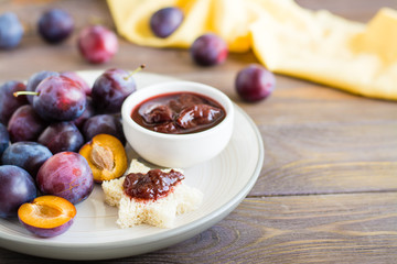 Appetizing bruschetta from fresh bread with plum jam and ripe berries of blue plums on a plate on a wooden table