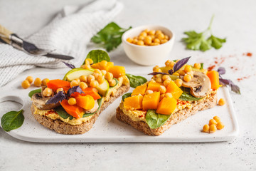 Vegan healthy sandwiches with hummus, chickpeas, baked vegetables and basil on white board.
