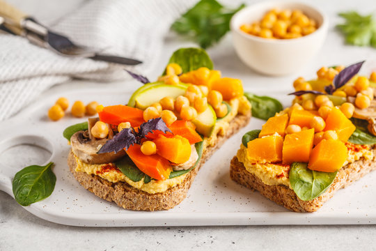 Vegan healthy sandwiches with hummus, chickpeas, baked vegetables and basil on white board.
