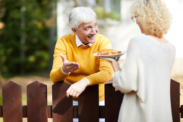 Blonde female giving her neighbour piece of homemade apple pie over wooden fence