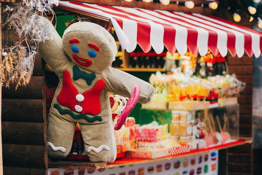 Gingerbread Cookie Man With Lollipop On Christmas Market Cabin. Winter Holiday Fair In European City Street. Candy Shop. Festive Decor And Illumination In City Center, Winter Holidays