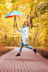 Young beautiful girl jumping in the autumn park with a colorful umbrella
