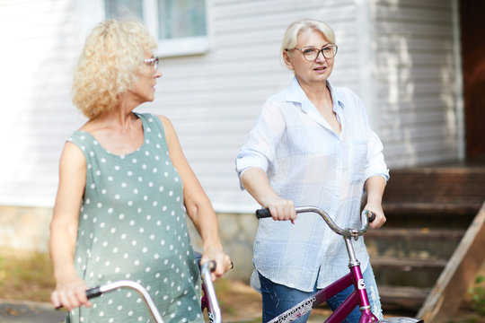 Two mature active females with bicycles having talk while chilling out on summer day