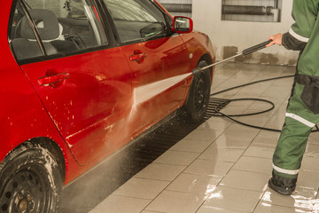 Red passenger car in the box at the car wash. Integrated washing under the pressure of water.