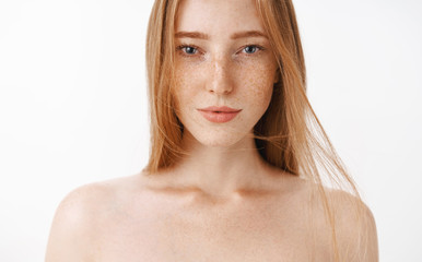 Close-up shot of attractive feminine naked redhead woman with freckles posing over gray background...