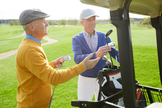 Two friendly mature men choosing golf clubs while going to play outdoor game at leisure