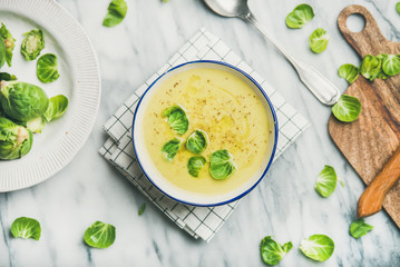 Flat-lay of seasonal brussels sprouts vegetable cream soup in bowl and fresh green brussel sprouts...