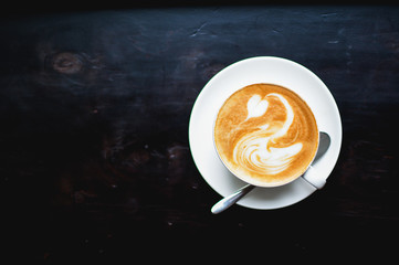 White cup of cappuccino with a white swan drawn on a brown coffee foam. Elegant coffee art. Concept background of cafe, rest, leisure, and romantic settings. View from above. Black table background