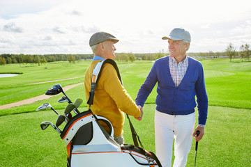 Naklejka premium Two friendly mature golf players shaking hands while greeting one another before game