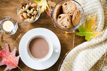 A cup of hot cocoa, nuts, cookies, candle and knitted plaid on a rustic wooden table.