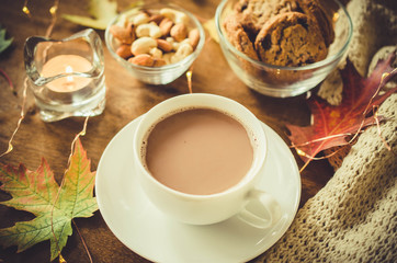 A cup of hot cocoa, nuts, cookies, candle and knitted plaid on a rustic wooden table.