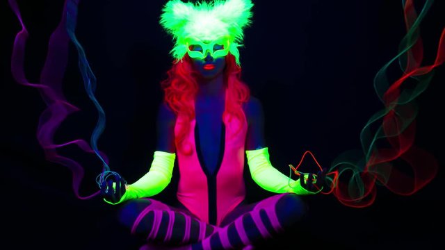 amazing female yoga instructor in lotus prayer pose wearing fluorescent clothing under UV black light