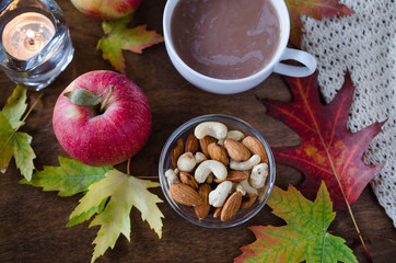 A cup of hot cocoa with knitted blanket, nuts, apples and autumn leaves. Thanksgiving day concept.