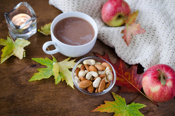 Fototapeta na wymiar A cup of hot cocoa with knitted blanket, nuts, apples and autumn leaves. Thanksgiving day concept.