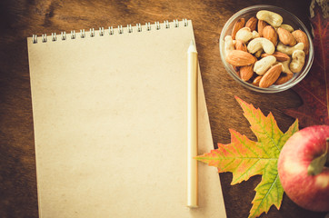 Blank brown notebook with nuts, apples and autumn leaves on wooden table. Autumn still life.