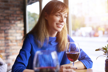 Beautiful woman drinking red wine with friends in cafe, portrait with wine glass near window. Vocation holidays bar concept..