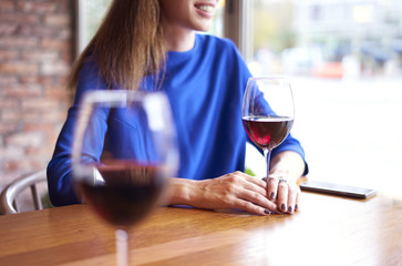 Woman drinking red wine with friends in cafe, focus on glass near window. Vocation holidays bar concept.