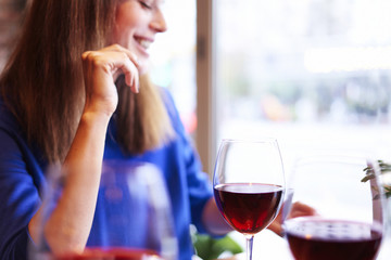 Woman drinking red wine with friends in cafe, focus on glass near window. Vocation holidays bar concept.