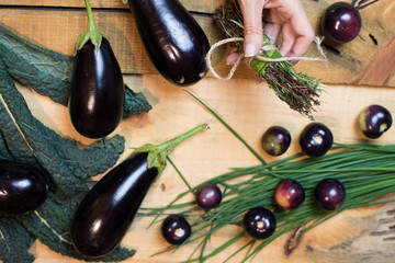 Woman making Bouquet garni with fresh herbs on elegant rustic wood background with healthy vegetables and super food kale