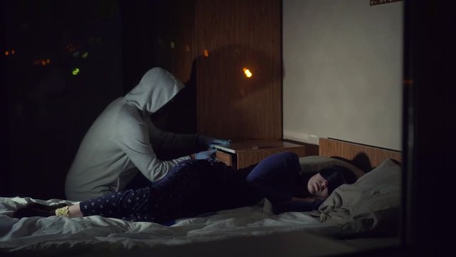 Thief criminal in a mask steals in the house where the girl sleeps