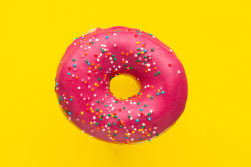 Donut pink with sprinkles isolated on yellow background, close-up